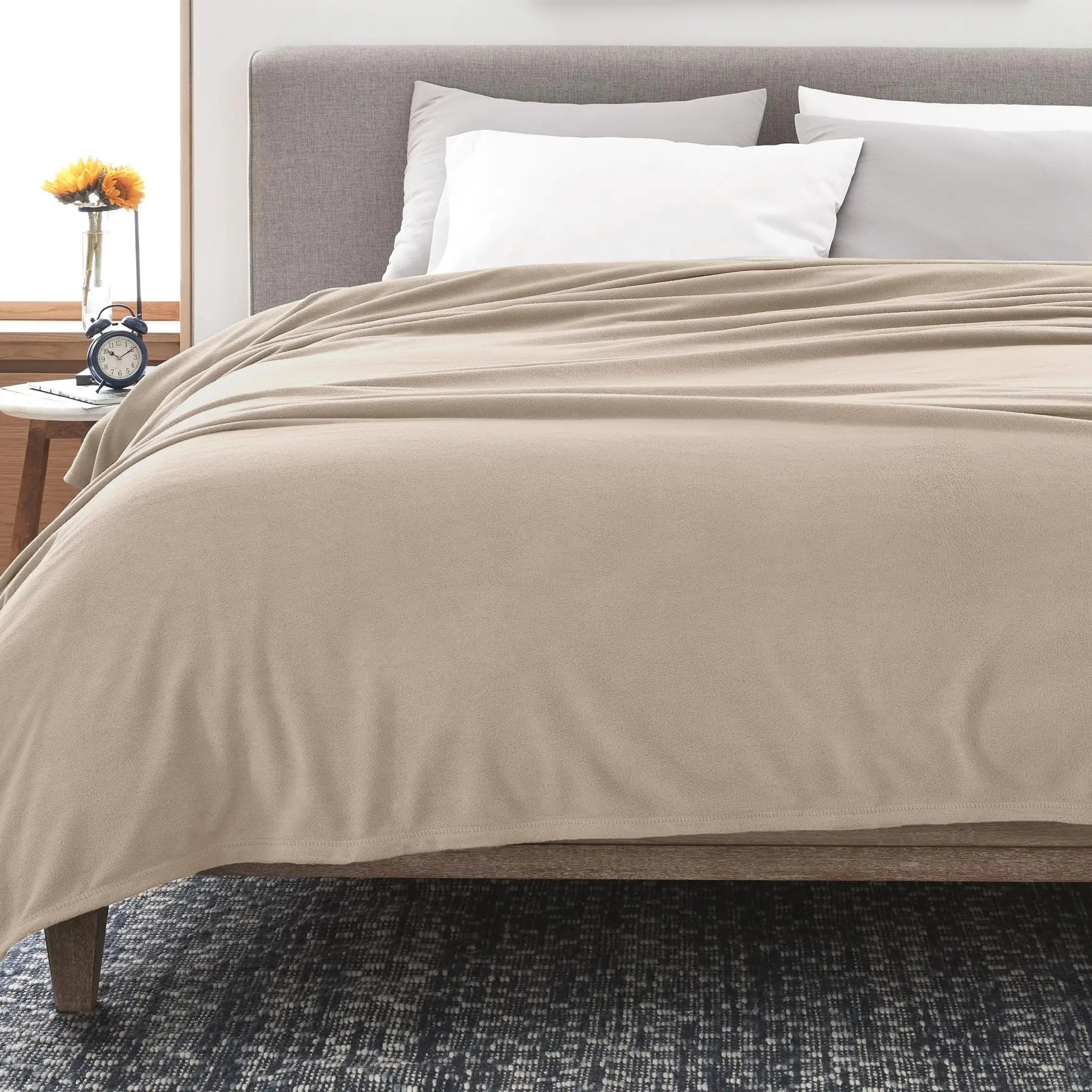 Beige blanket on a bed with white pillows in a bedroom setting.