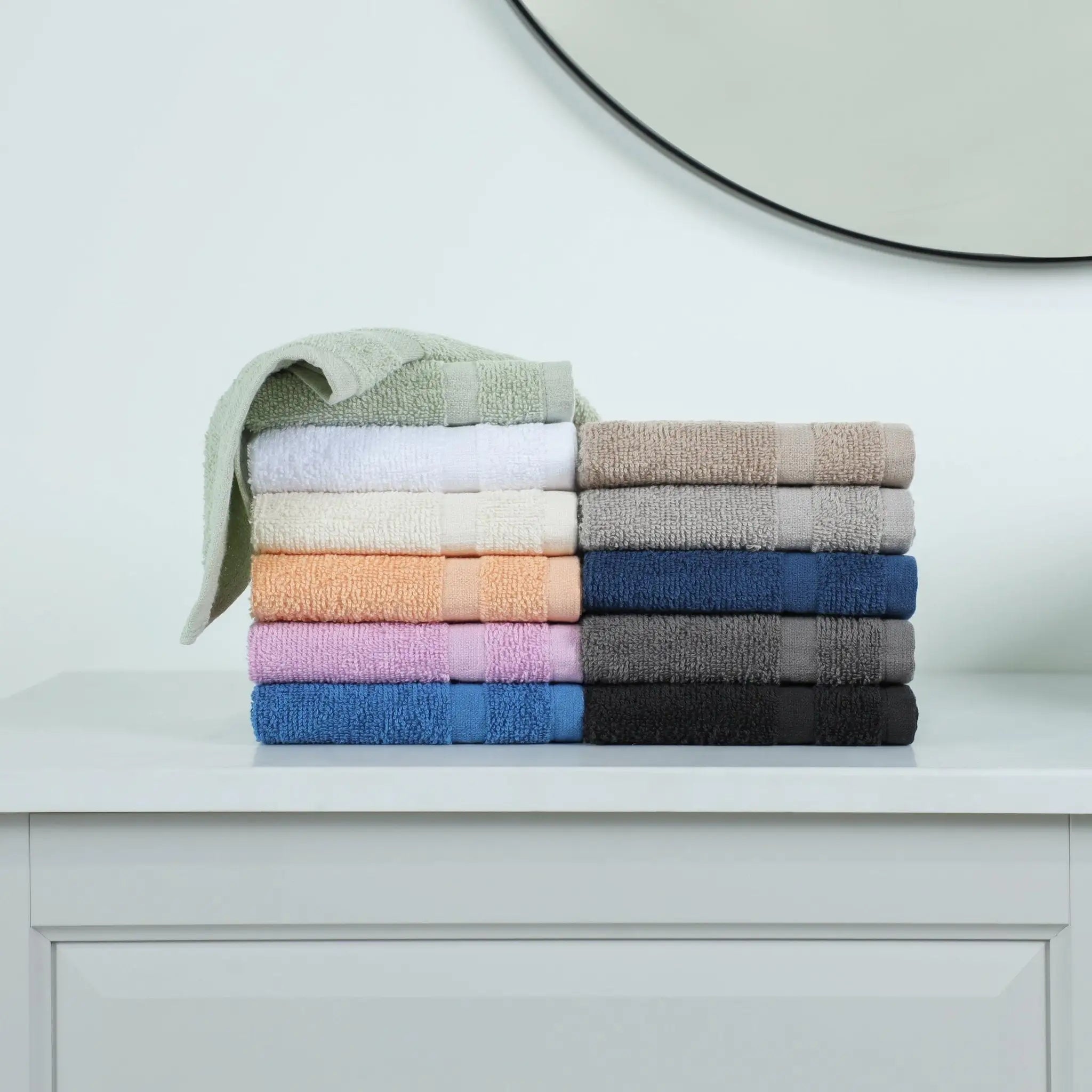 Stack of folded washcloths in various colors on a white surface with a mirror in the background.