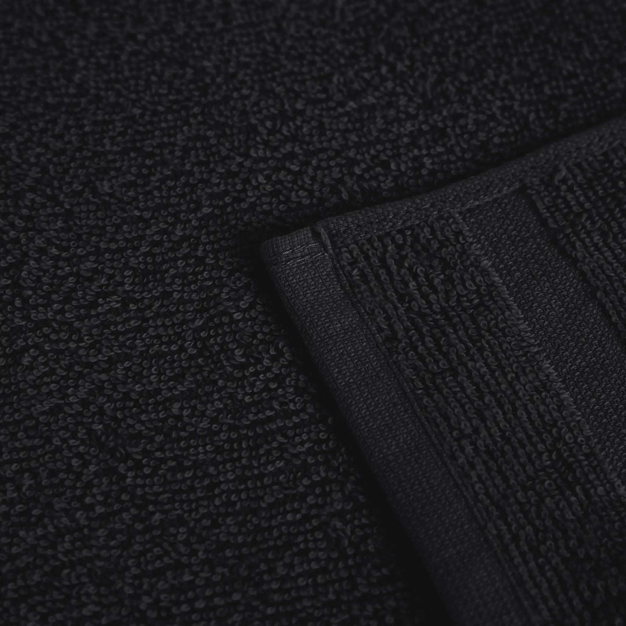 Close-up of a black textured fabric product, showing a looped terry surface and a folded ribbed edge.