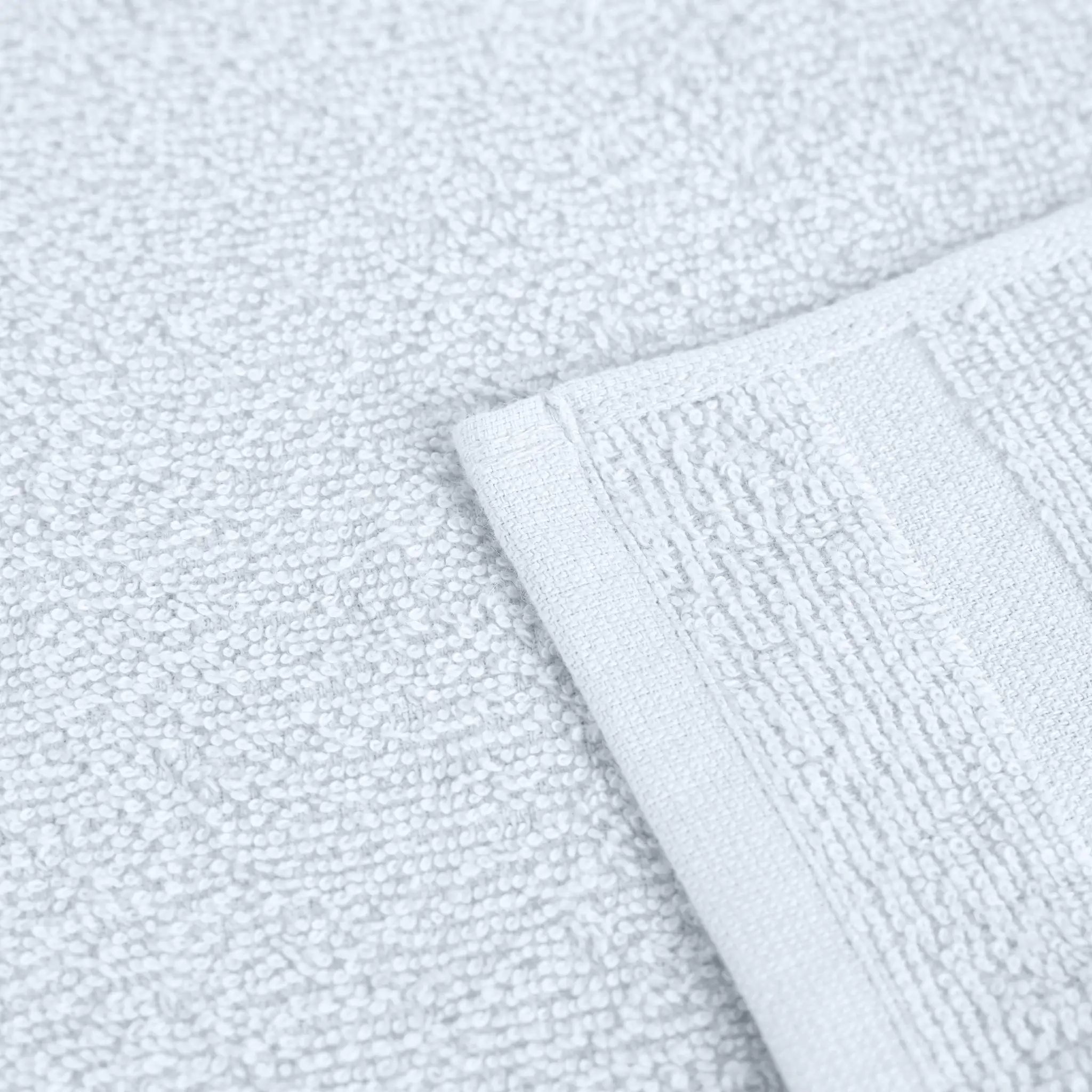 Close-up of a white textured washcloth with a folded corner showing its terry cloth weave and stitched border.