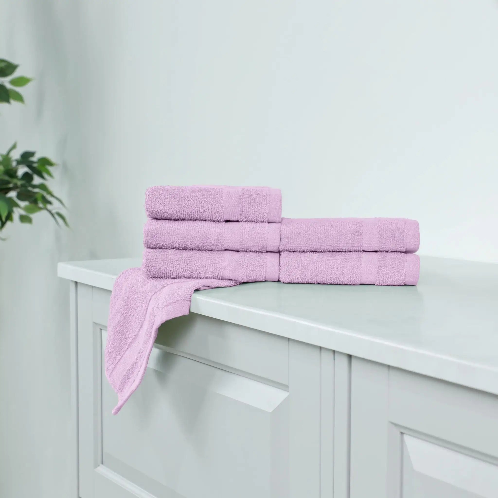 A set of folded lilac washcloths, arranged on a white vanity cabinet with one washcloth draped over the edge.