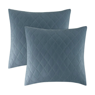 Two square quilted throw pillows in a muted slate blue color, arranged with one slightly behind the other on a plain white background.