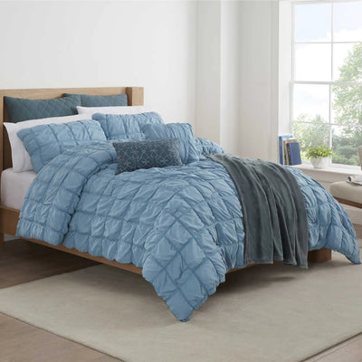 Blue textured comforter set on a bed in a bright bedroom with large windows.