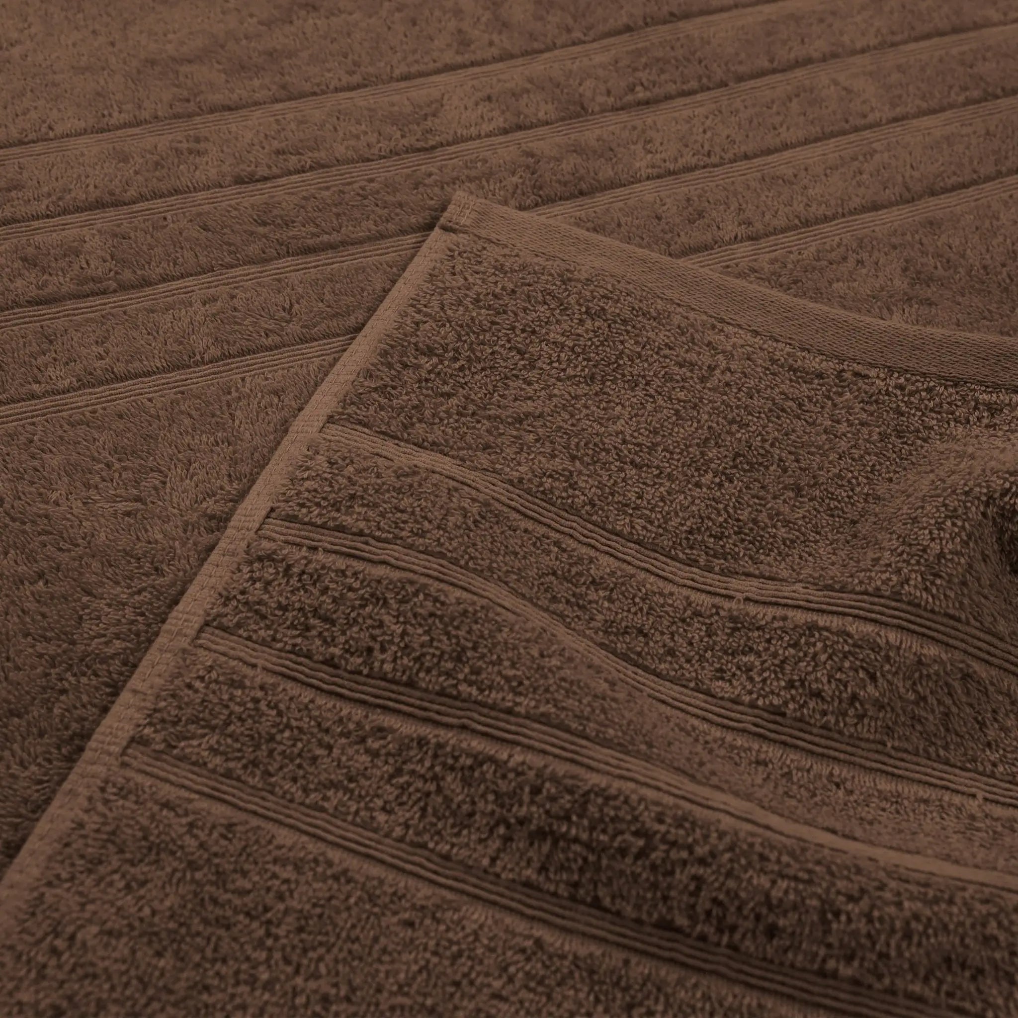 A close-up of a chocolate-colored bath towel with horizontal ribbed stripes, folded over to show its plush terry fabric.