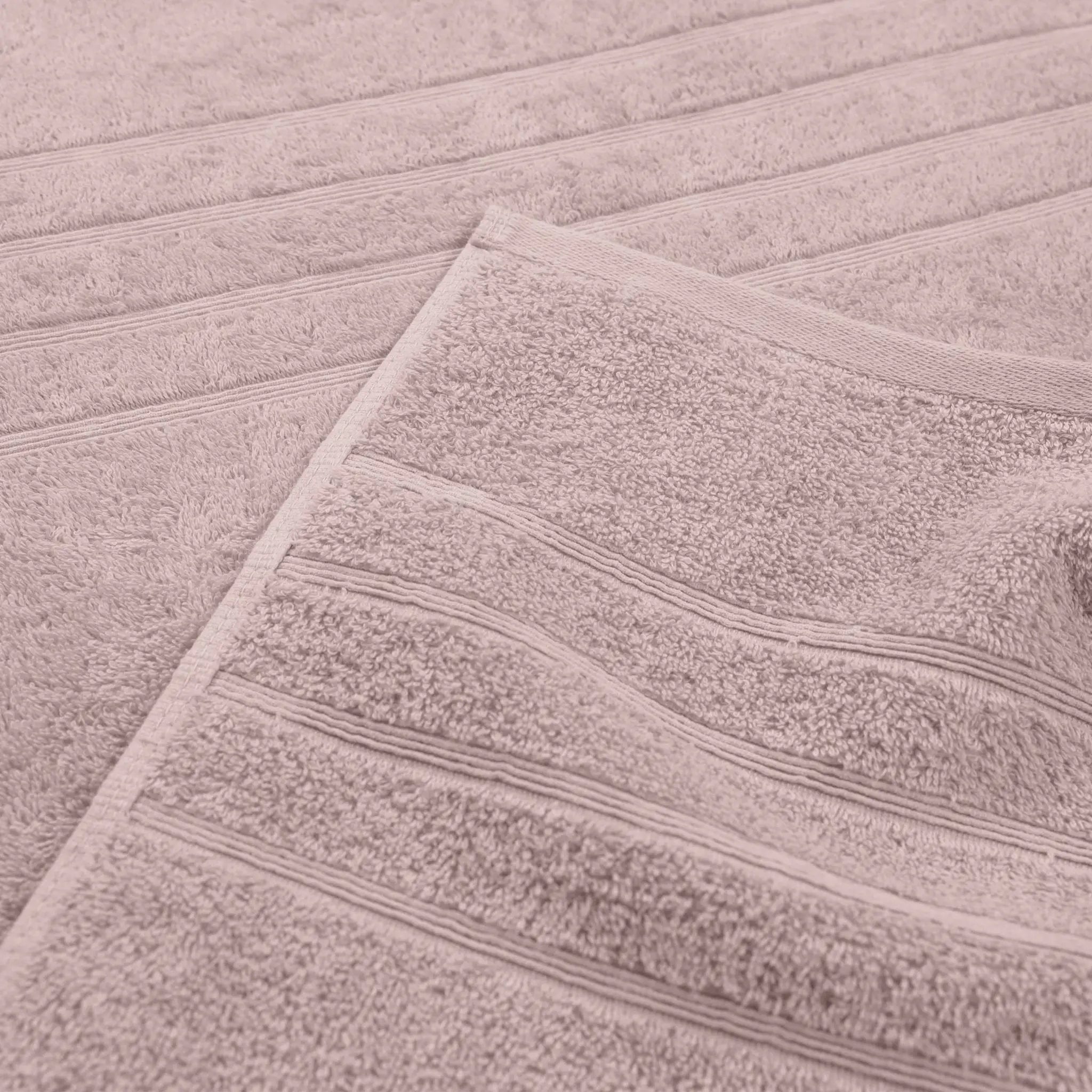 A close-up of a soft, textured bath towel in a pink color, folded over to show its looped terry texture and stitched border.