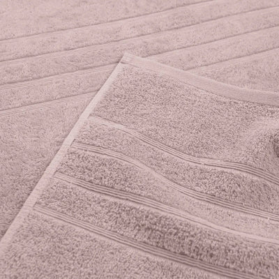 A close-up of a soft, textured bath towel in a pink color, folded over to show its looped terry texture and stitched border.