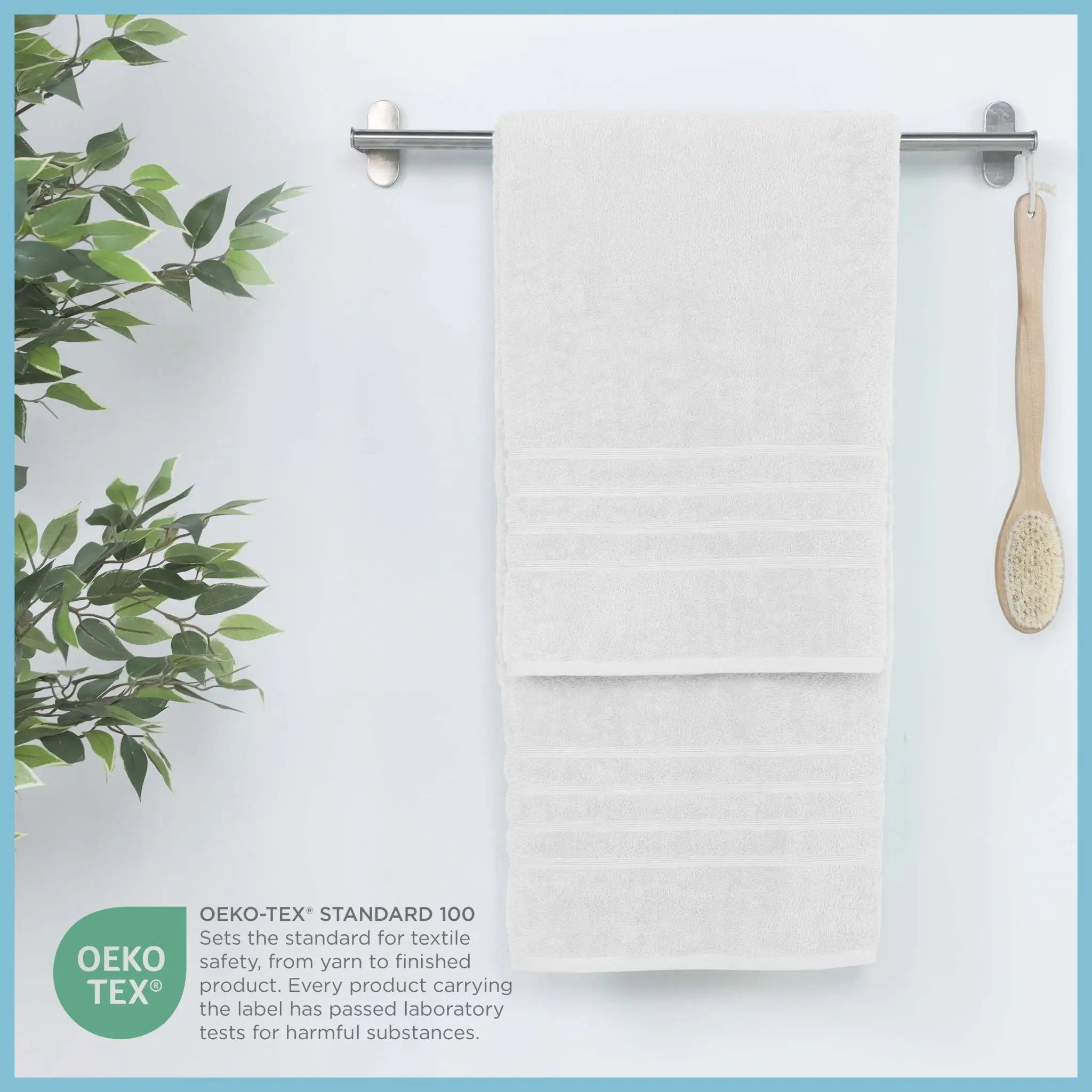 White bath sheet hanging on a rack with a plant and brush, featuring OEKO-TEX certification.