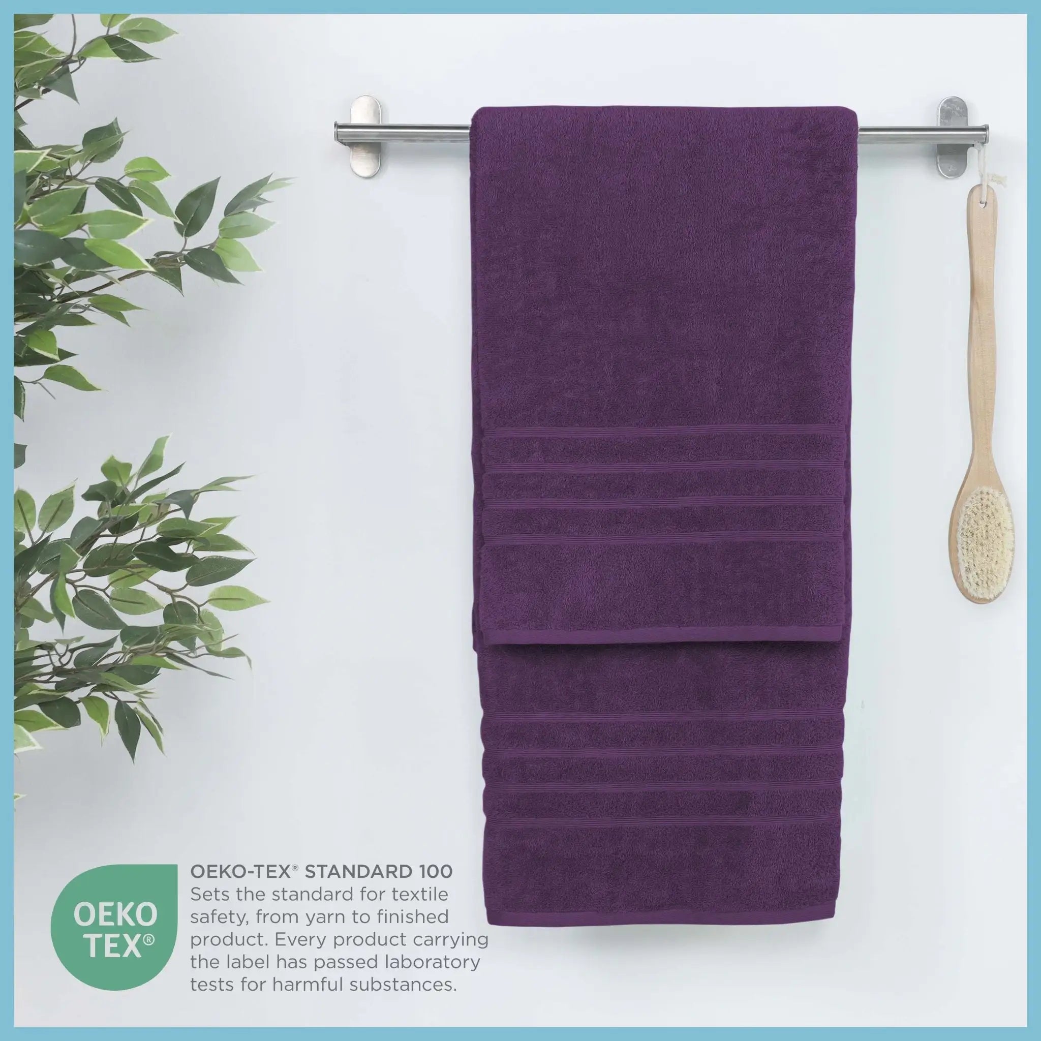 Purple bath sheets hanging on a rack with a plant and brush in the background, featuring OEKO-TEX certification.