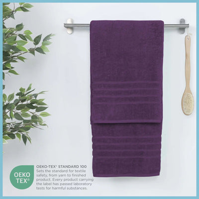 Purple bath sheets hanging on a rack with a plant and brush in the background, featuring OEKO-TEX certification.