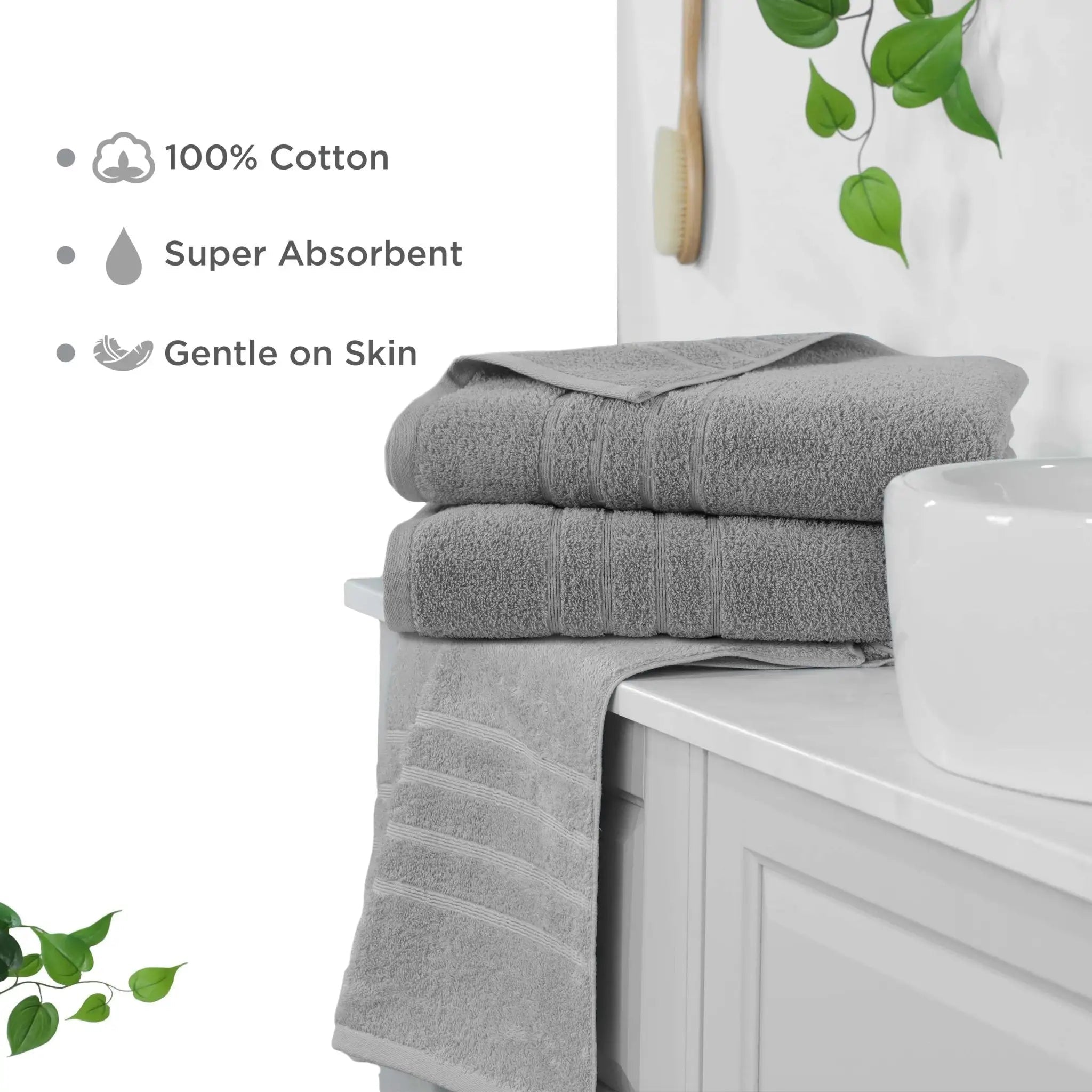 Two folded gray cotton bath sheets stacked on a white bathroom vanity next to a white sink, with a third towel draped over the edge. Text on the left highlights the towels' features: 100% cotton, super absorbent, and gentle on skin.