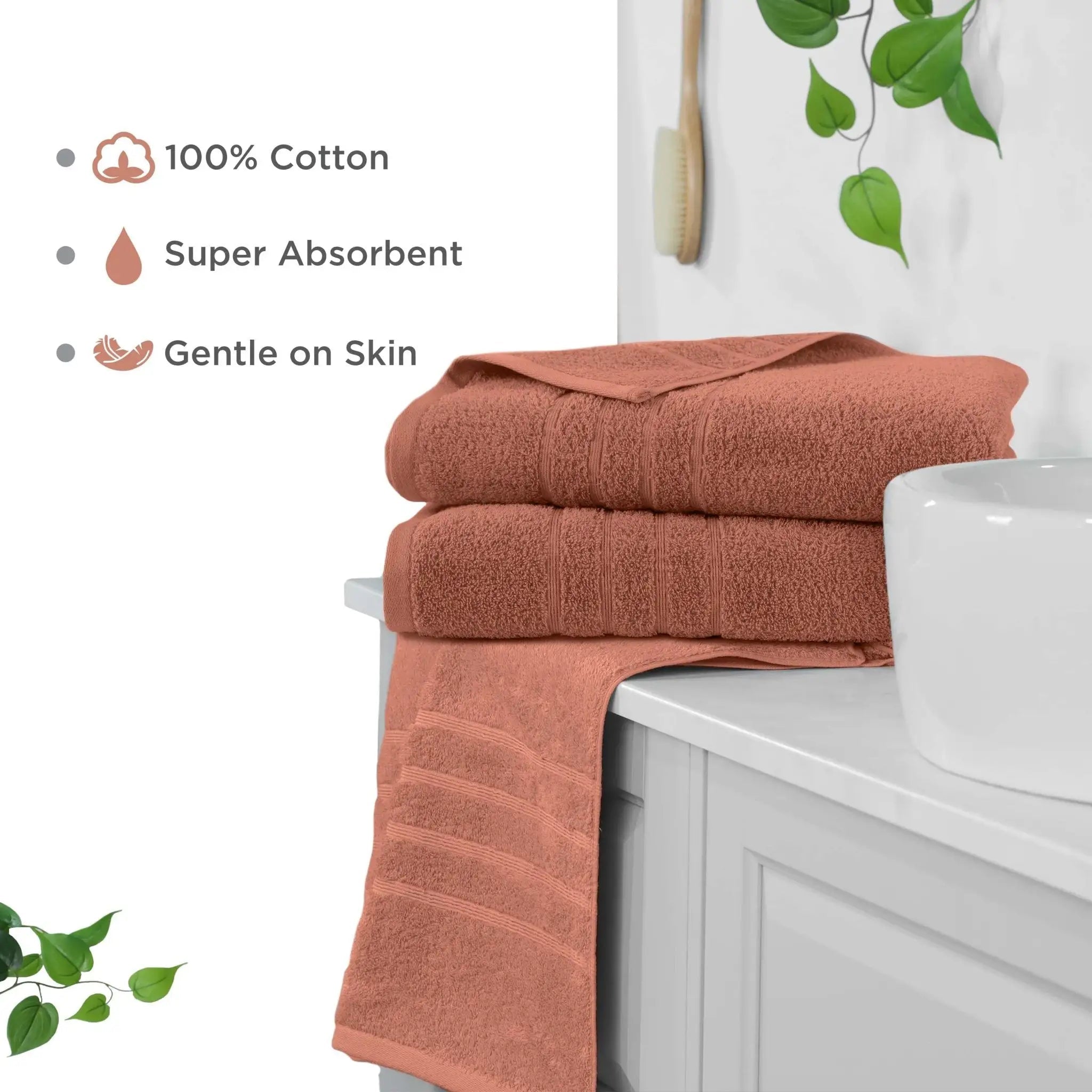 Two folded terracotta-colored cotton bath sheets stacked on a white bathroom vanity next to a white sink, with a third towel draped over the edge. Text on the left highlights product features: 100% cotton, super absorbent, and gentle on skin.