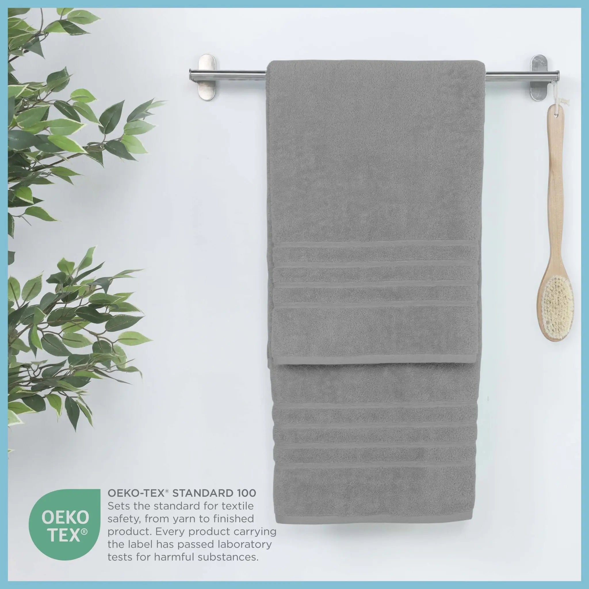 Gray bath sheet hanging on a rack with a plant and brush on a white background, featuring OEKO-TEX certification.