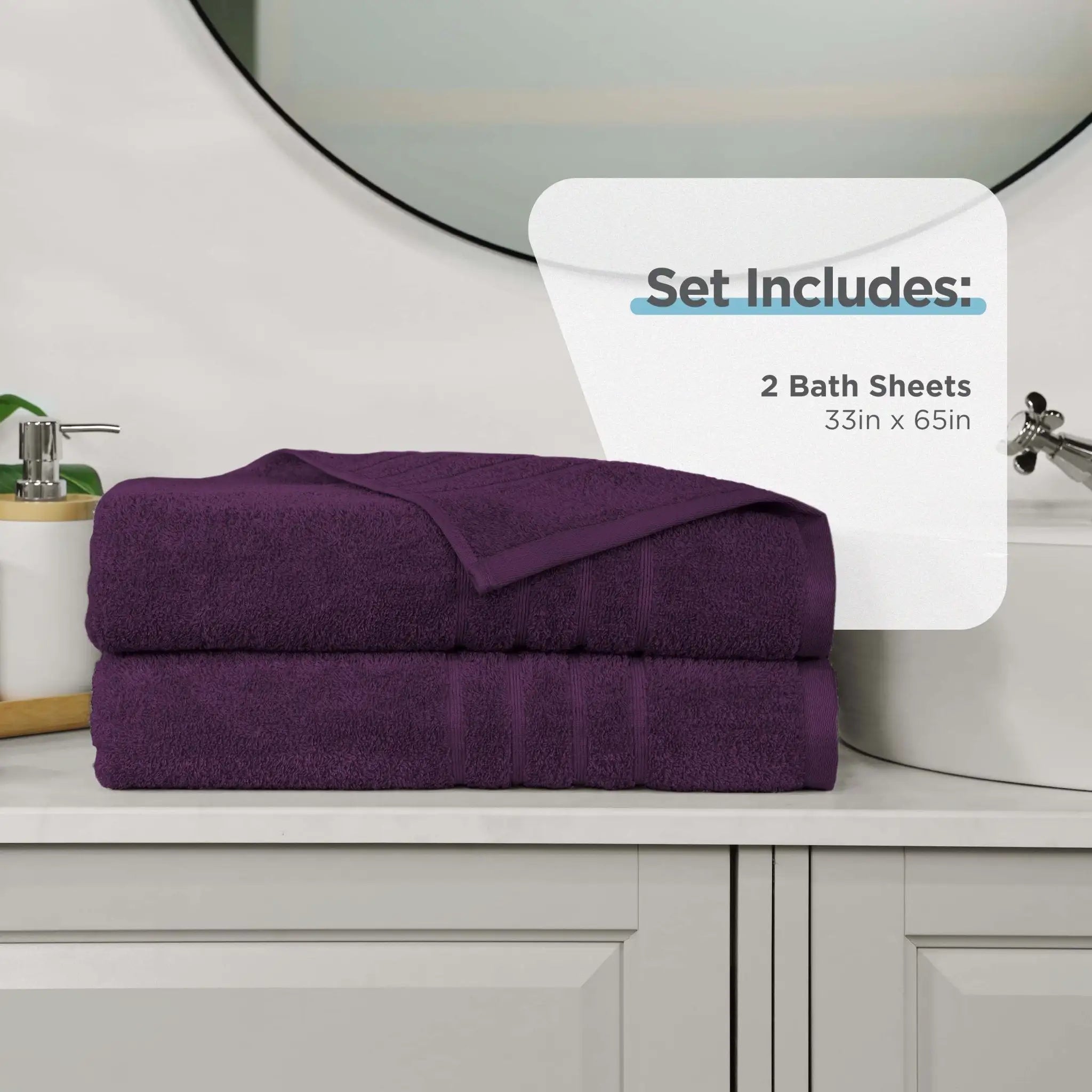 Two folded purple bath sheets stacked on a bathroom counter, with a white sign reading 'Set Includes: 2 Bath Sheets 33in x 65in' in front of a sink and mirror.