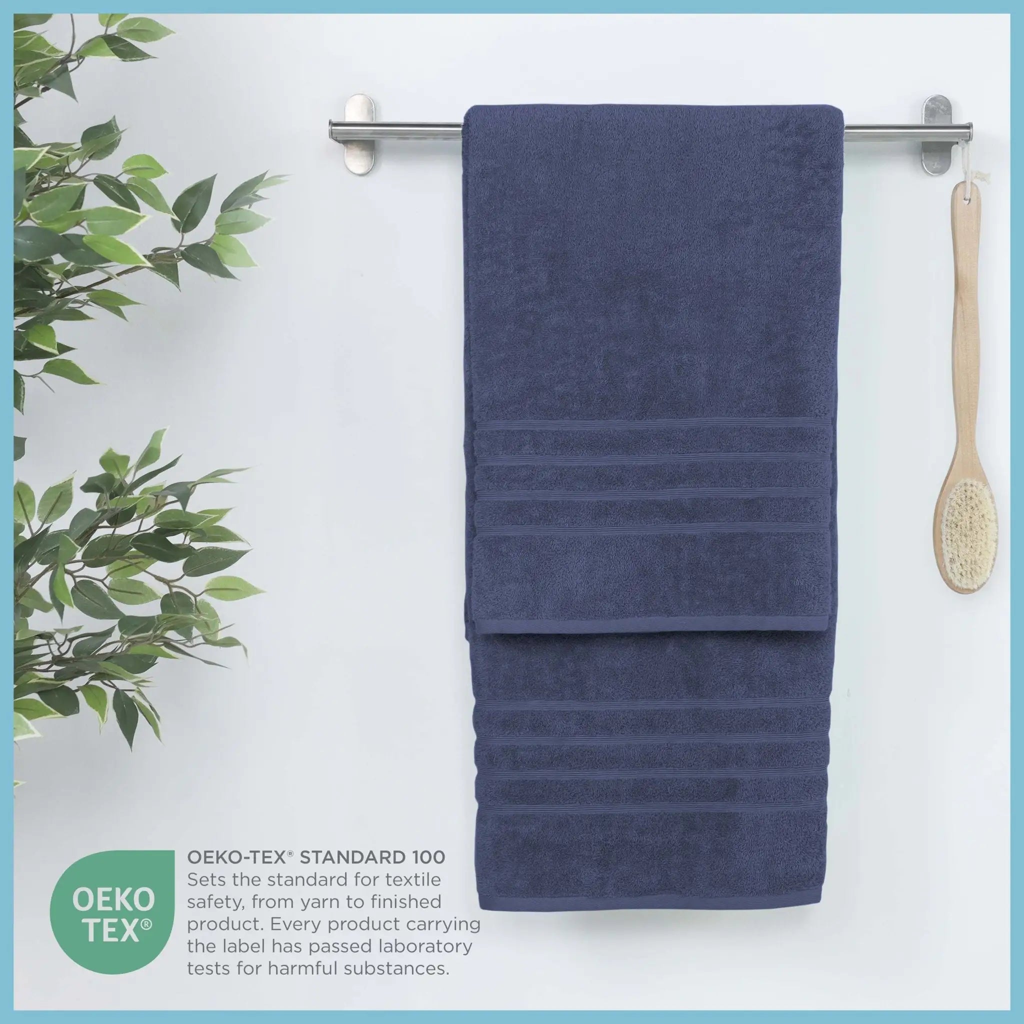 Estate blue bath sheet hanging on a rack with a plant and brush in the background, featuring OEKO-TEX certification.