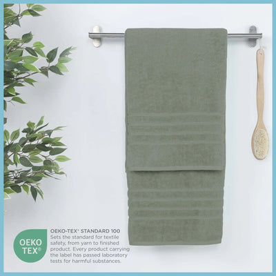 Sage bath sheet hanging on a rack with a plant and brush on a white background, featuring OEKO-TEX certification.