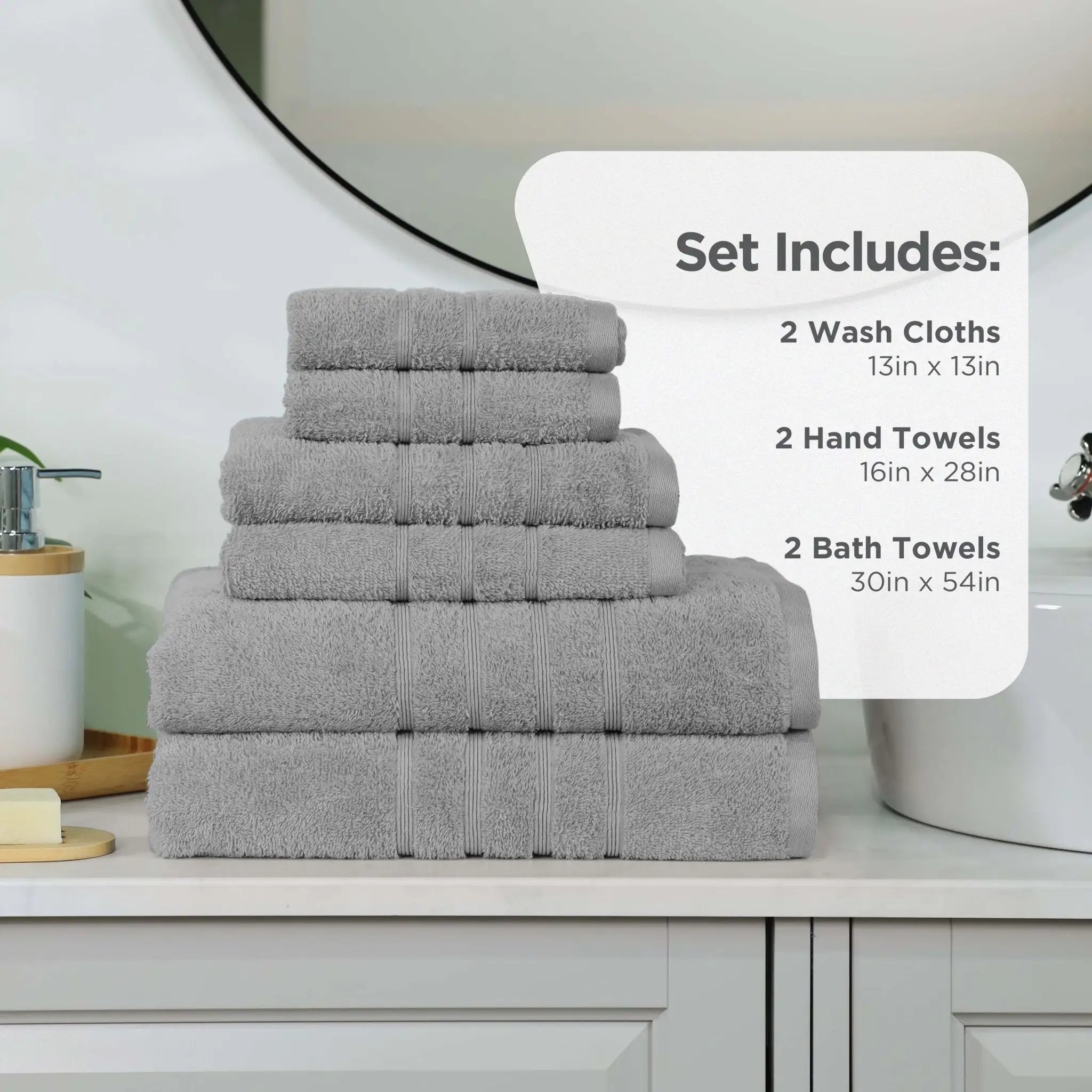 A stack of gray towel set displayed on a bathroom counter, with an informational overlay that reads 'Set Includes: 2 Wash Cloths 13in x 13in, 2 Hand Towels 16in x 28in, 2 Bath Towels 30in x 54in.'.