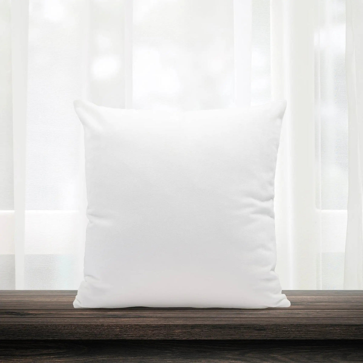 White pillow on a wooden surface with white curtains in the background