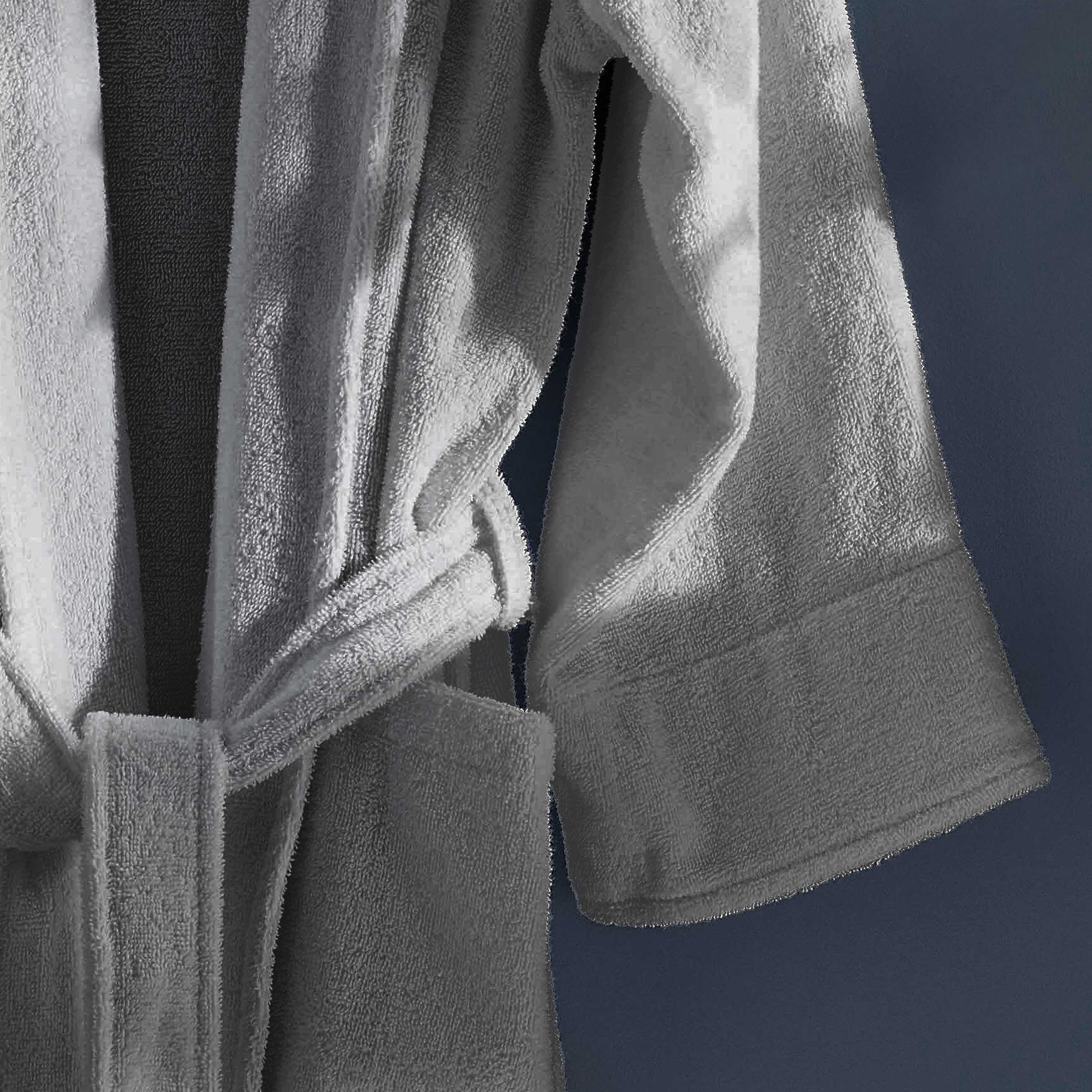 Light gray terry bath robe with a belt and wide sleeves, hanging against a dark background.