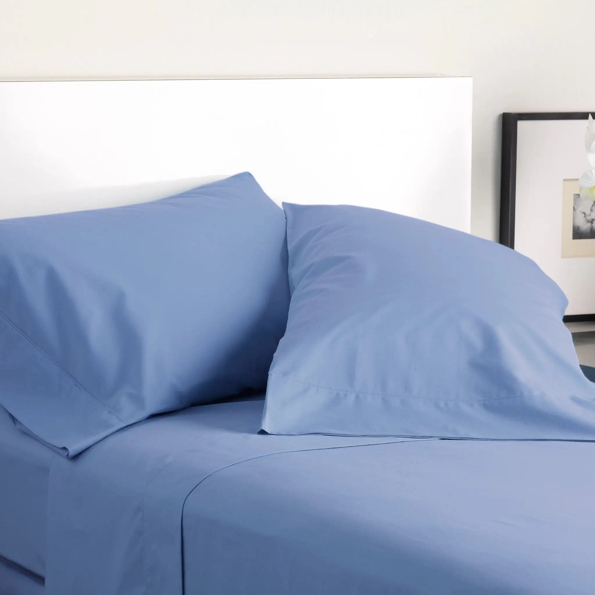 Blue bed sheets and pillows on a bed with a white headboard.