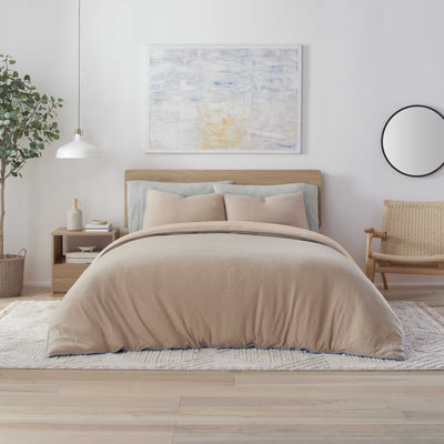 Beige comforter set on a bed with light blue and beige pillows, a wooden headboard, and a minimalist decor.