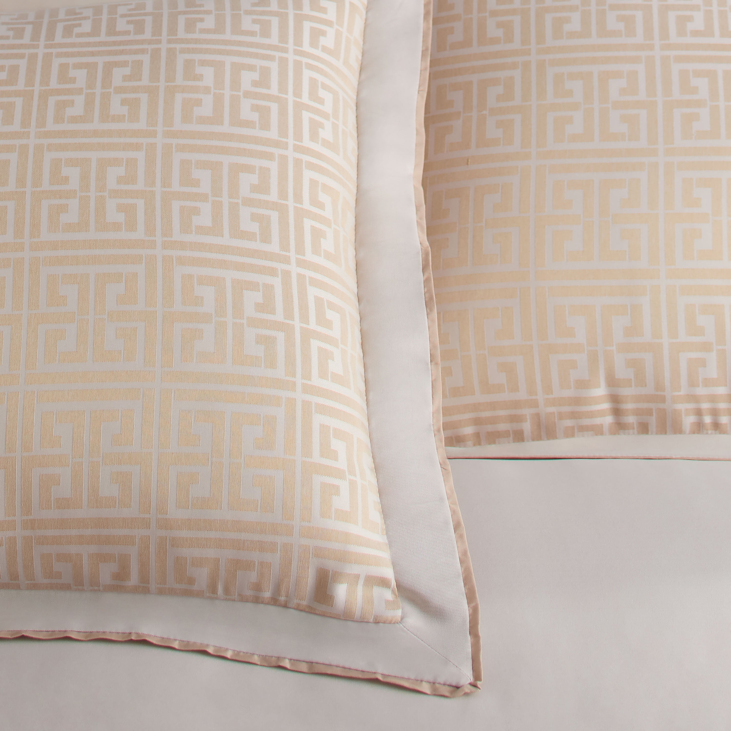 Two decorative pillows with a geometric pattern in soft beige and cream colors, featuring a satin-like finish.