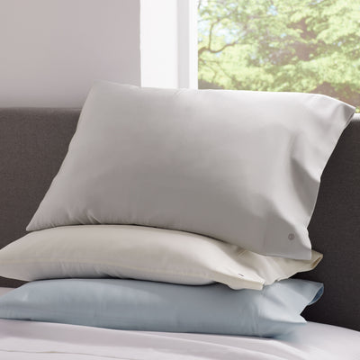 Two satin pillowcases in gray and cream stacked on a bed with a light blue pillow beneath.