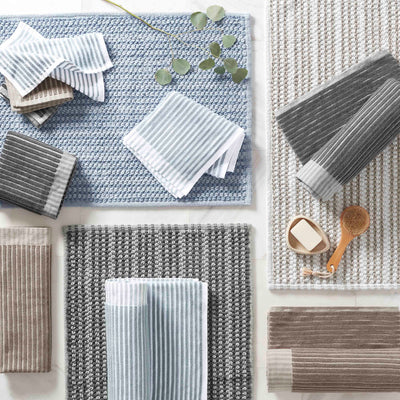 Various striped towels in blue, gray, and beige arranged on textured mats with a few decorative items.