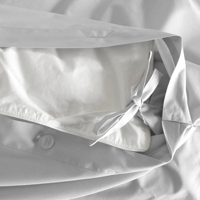 Close-up of a light gray comforter with a tied closure and button detail on the edge.