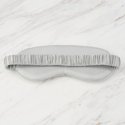 Gray satin eye mask with a ruffled elastic band, resting on a marble surface.