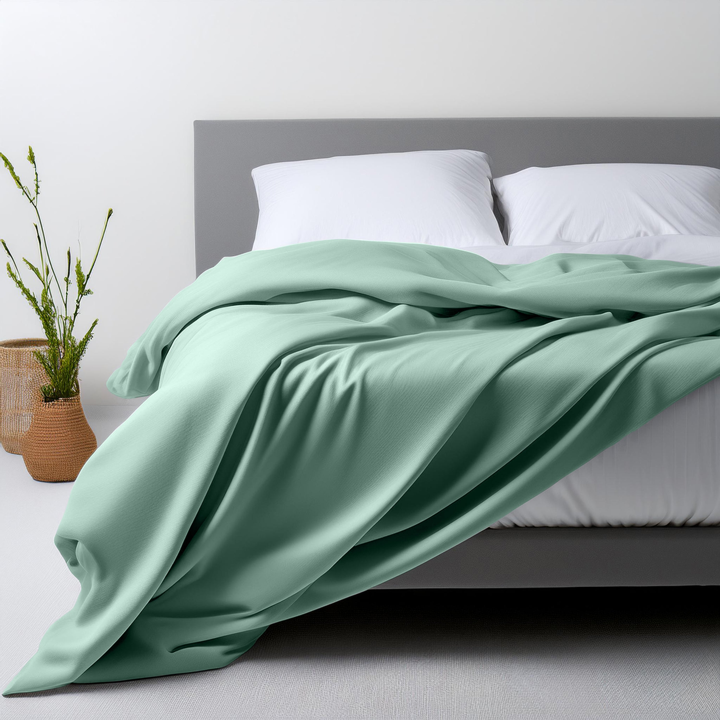 Light green sheet set draped over a bed with white pillows and a plant in a woven basket nearby.