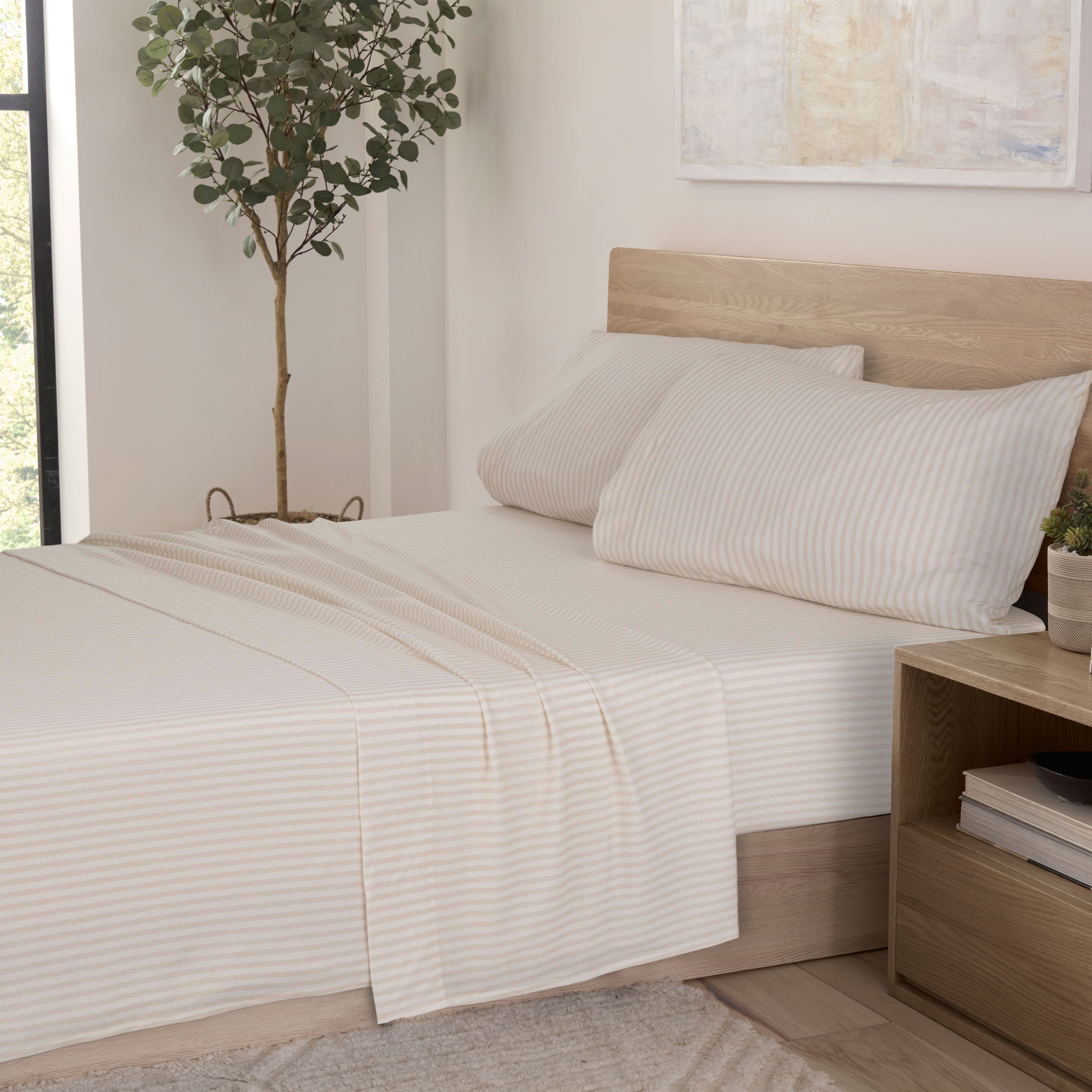Soft taupe sheet set with subtle stripes, paired with two matching pillowcases on a bed in a bright room.