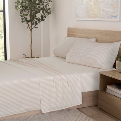 Soft taupe sheet set with subtle stripes, paired with two matching pillowcases on a bed in a bright room.