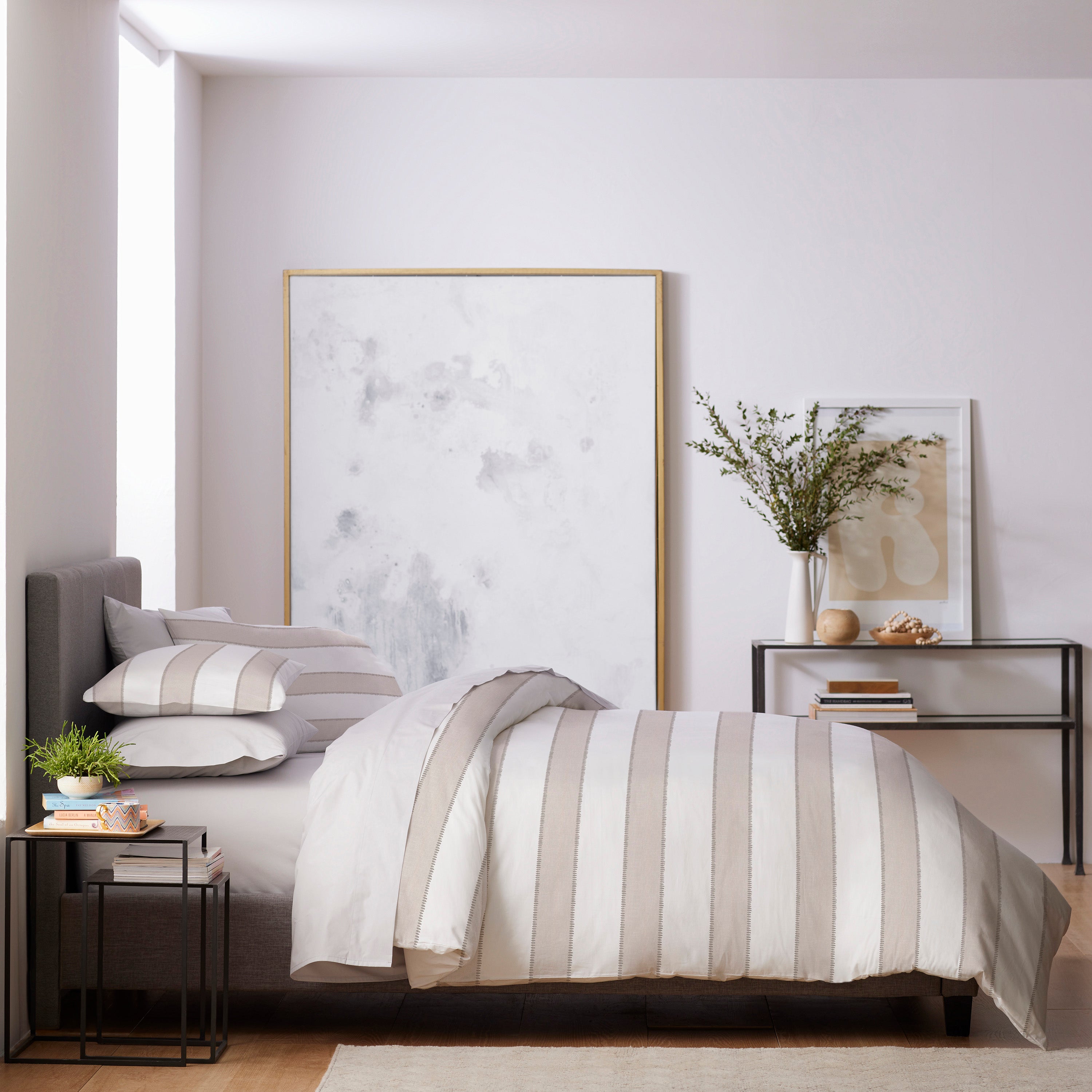 Duvet set with striped design on a bed, accompanied by decorative pillows and a nightstand with plants and decor.