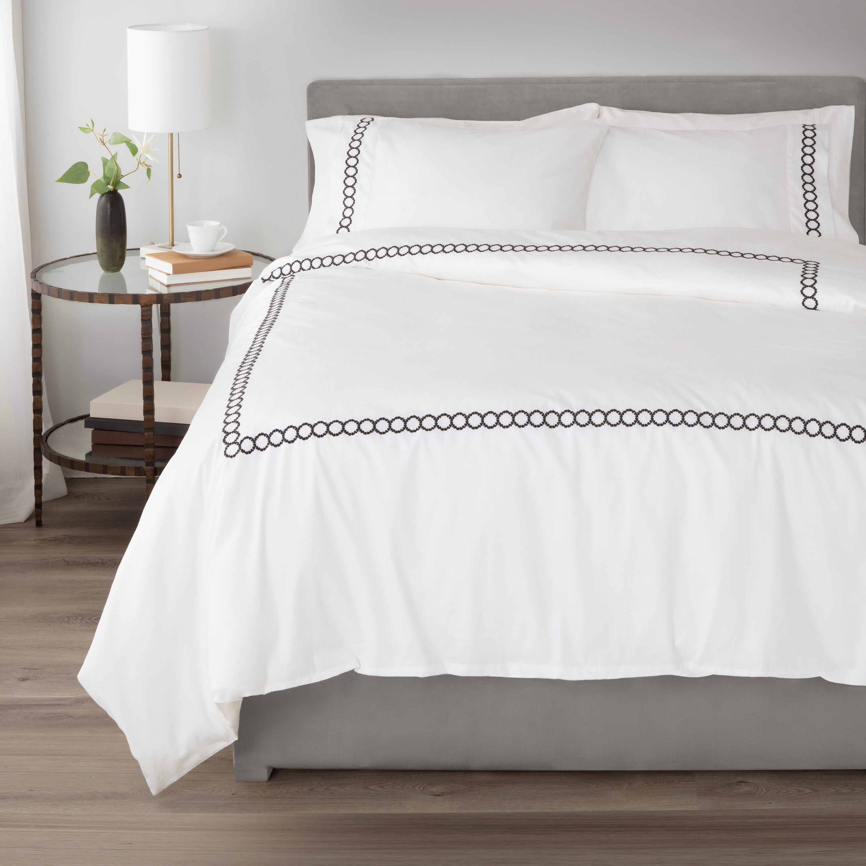 White comforter set with black circular embroidery, paired with matching pillowcases on a gray bed frame.