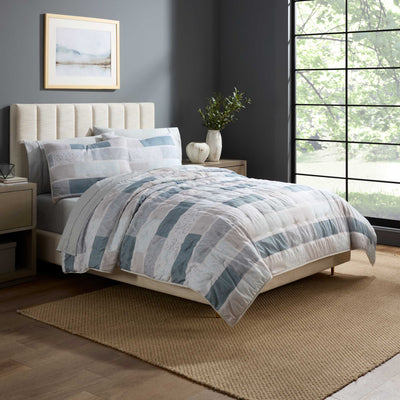 Quilt set featuring a patchwork design in shades of blue and gray, displayed on a bed with matching pillows.
