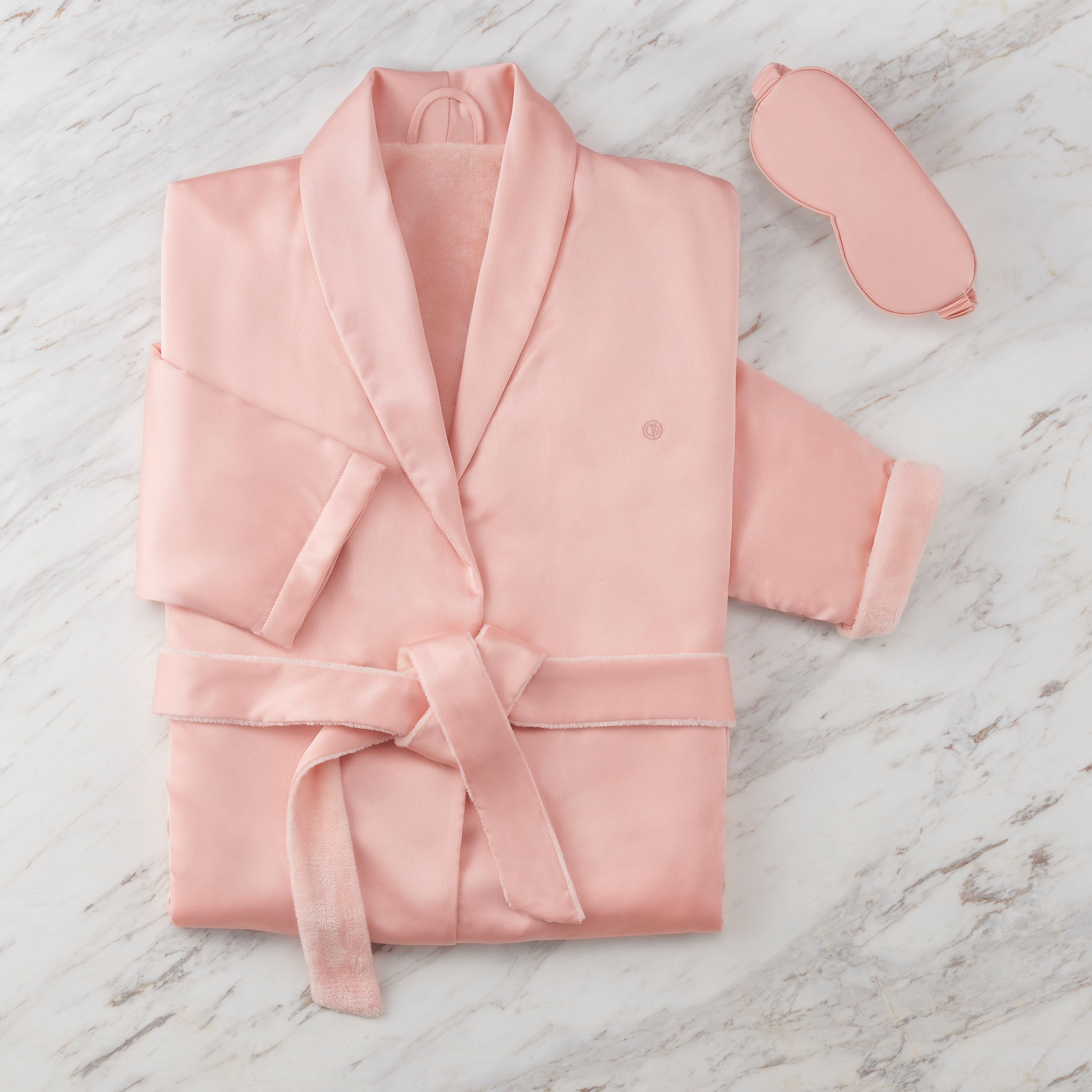 Pink satin robe with a matching eyemask, displayed on a marble surface.