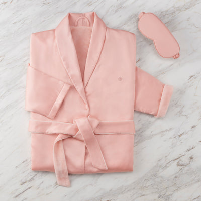 Pink satin robe with a matching eyemask, displayed on a marble surface.