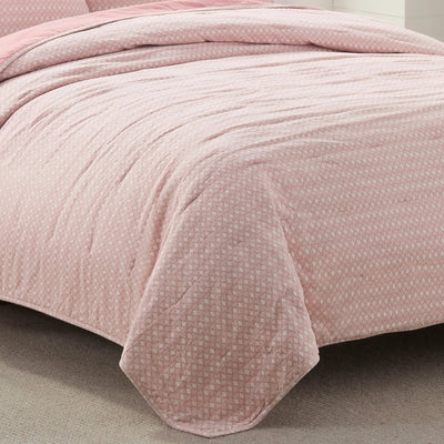 Pink textured quilt on a bed with a neutral background