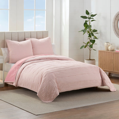 Pink quilt set on a bed in a bright bedroom.