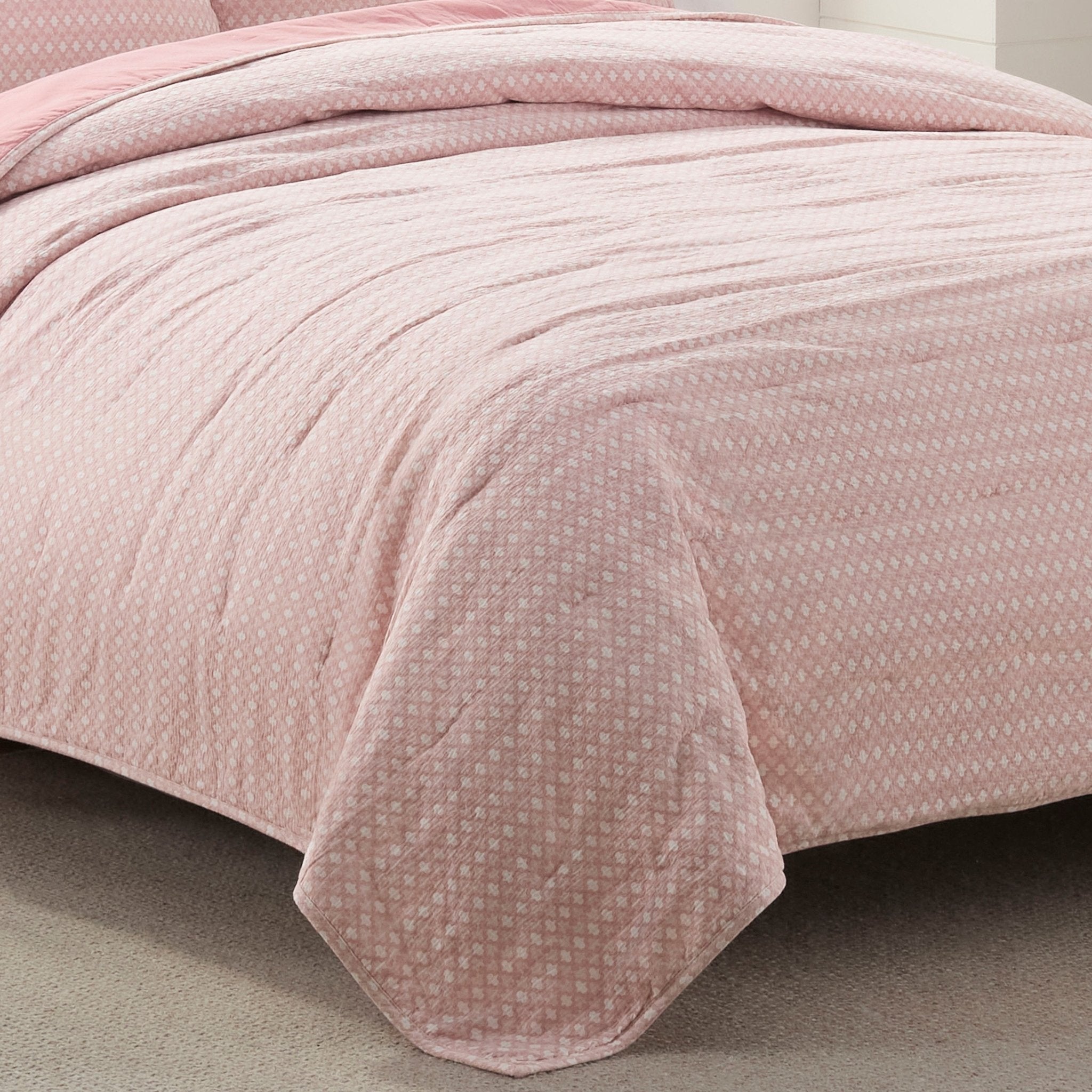 Pink textured quilt on a bed with a neutral background