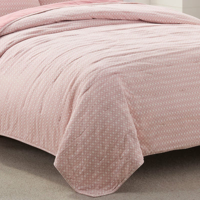 Pink textured quilt on a bed with a neutral background
