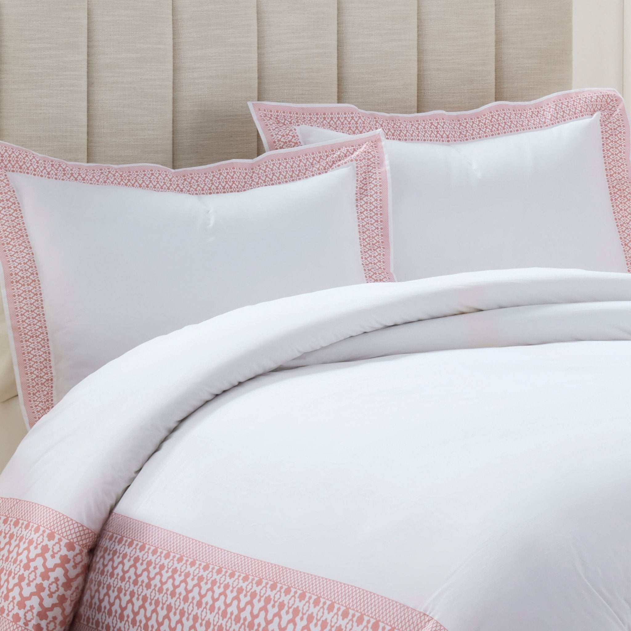 White bedding set with pink trim on a bed against a beige headboard.