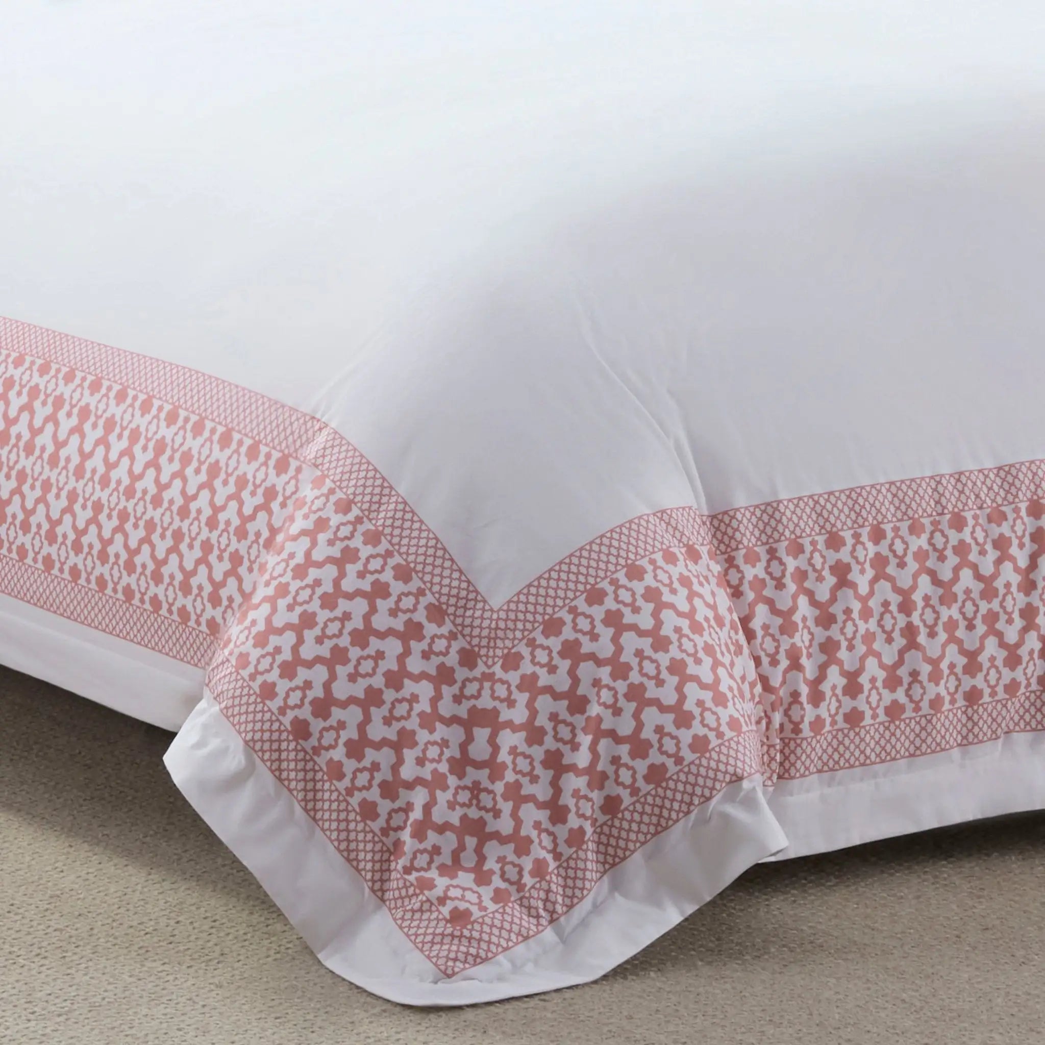 Close-up of a white comforter with pink geometric patterned trim on a beige surface.