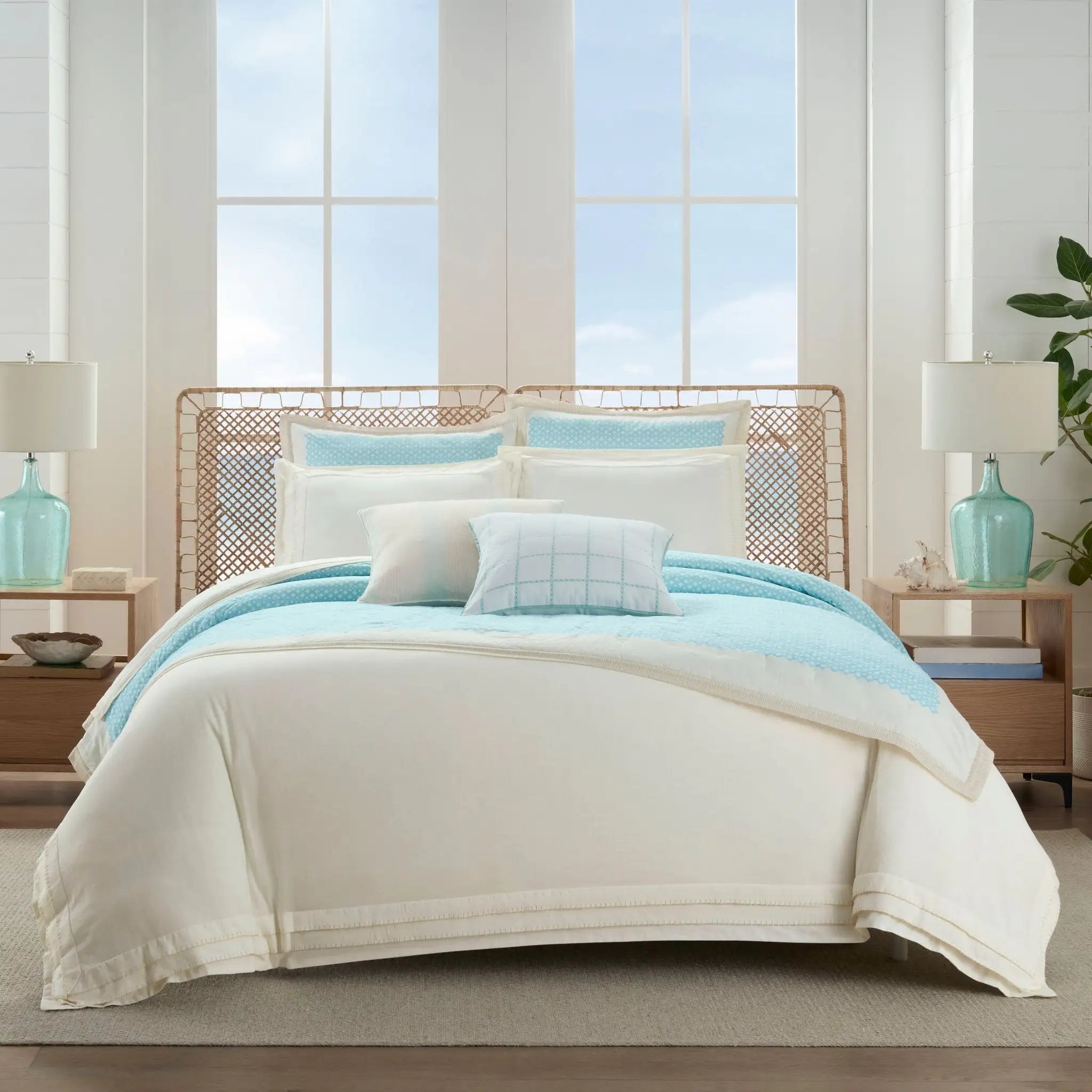 Bedroom with a bed featuring light blue and white bedding, nightstands with lamps, and large windows.
