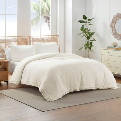 Neatly made bed with white comforter set in a bright bedroom