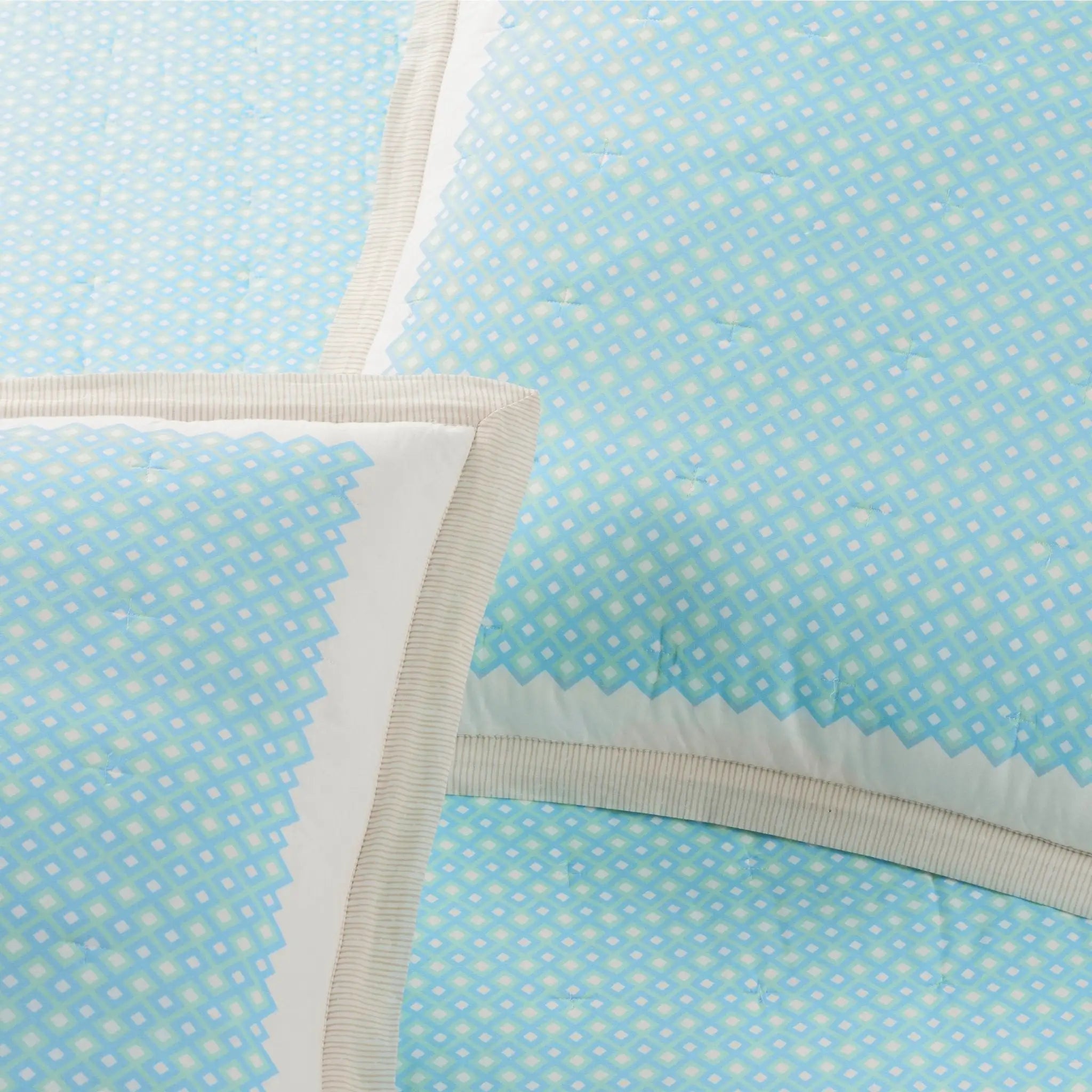 Light blue quilt with a repeating white and pale blue geometric pattern, cream zigzag borders, and ribbed trim.