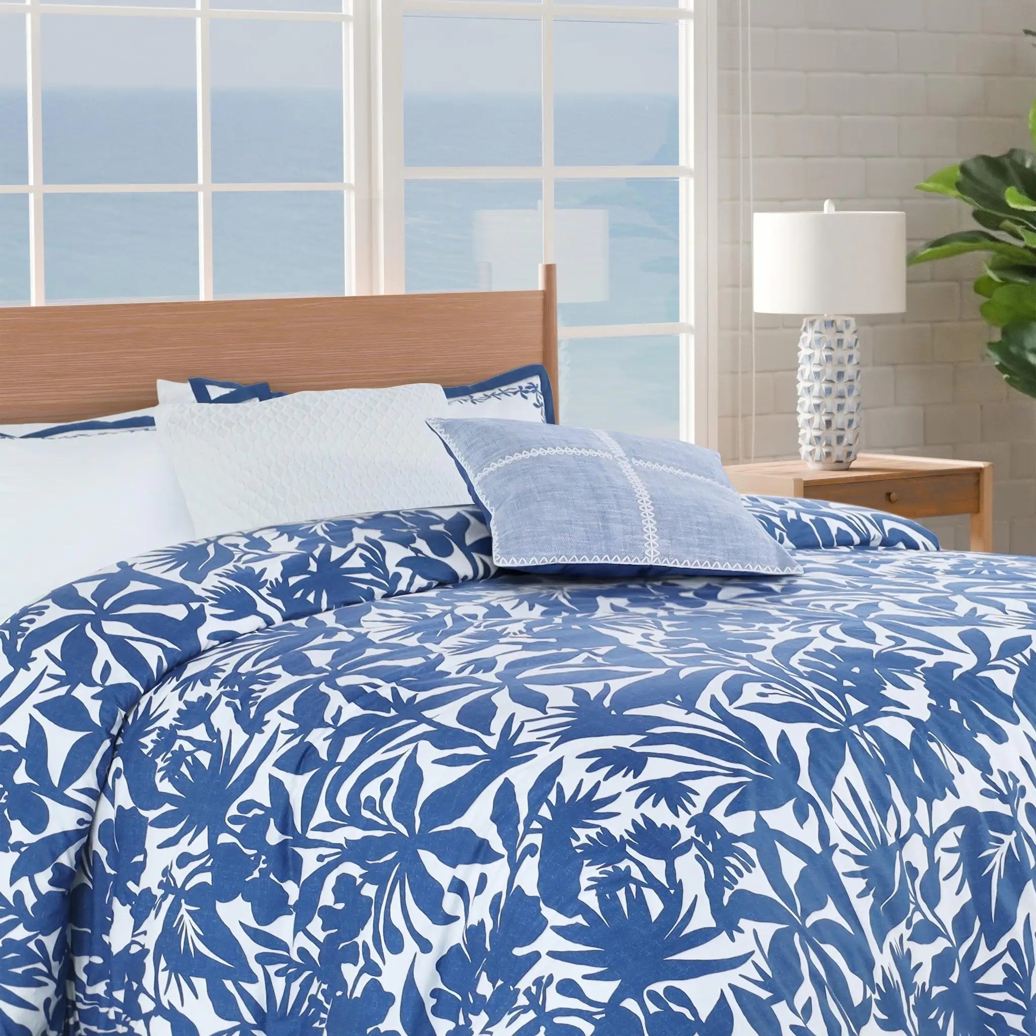 Blue and white floral comforter set on a bed with a window view.