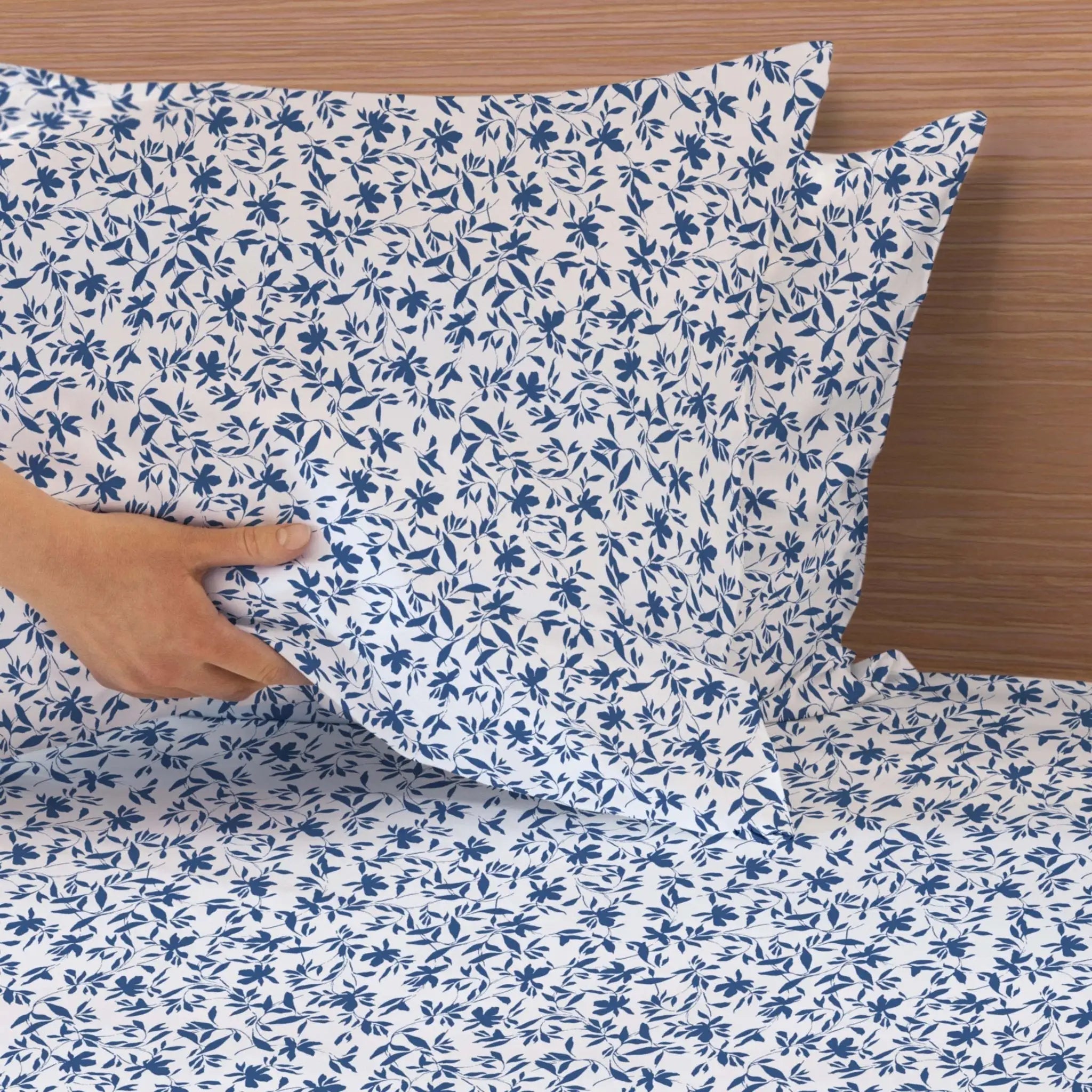 Blue floral patterned fabric being held over a wooden surface