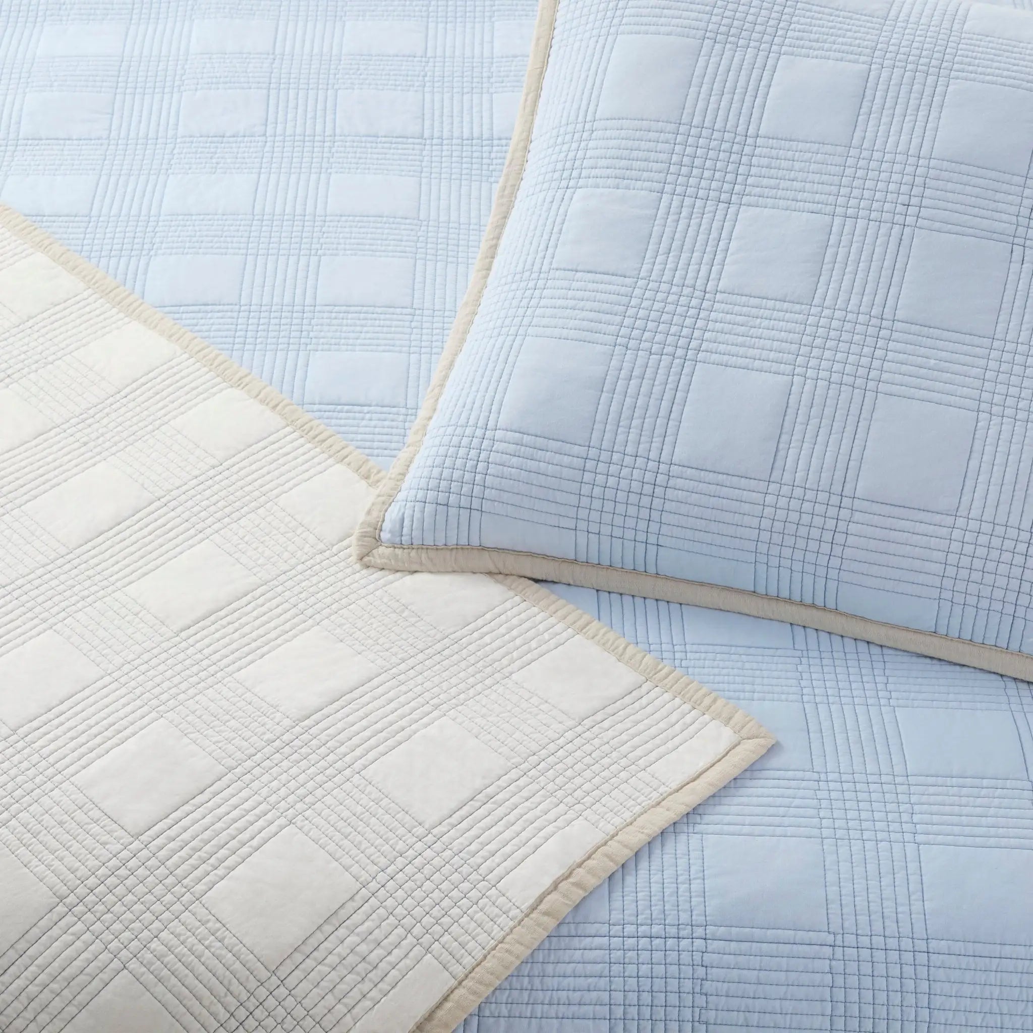 A close-up of quilt showing a light blue plaid sheet matching euro, alongside a reverse side cream-colored quilt.