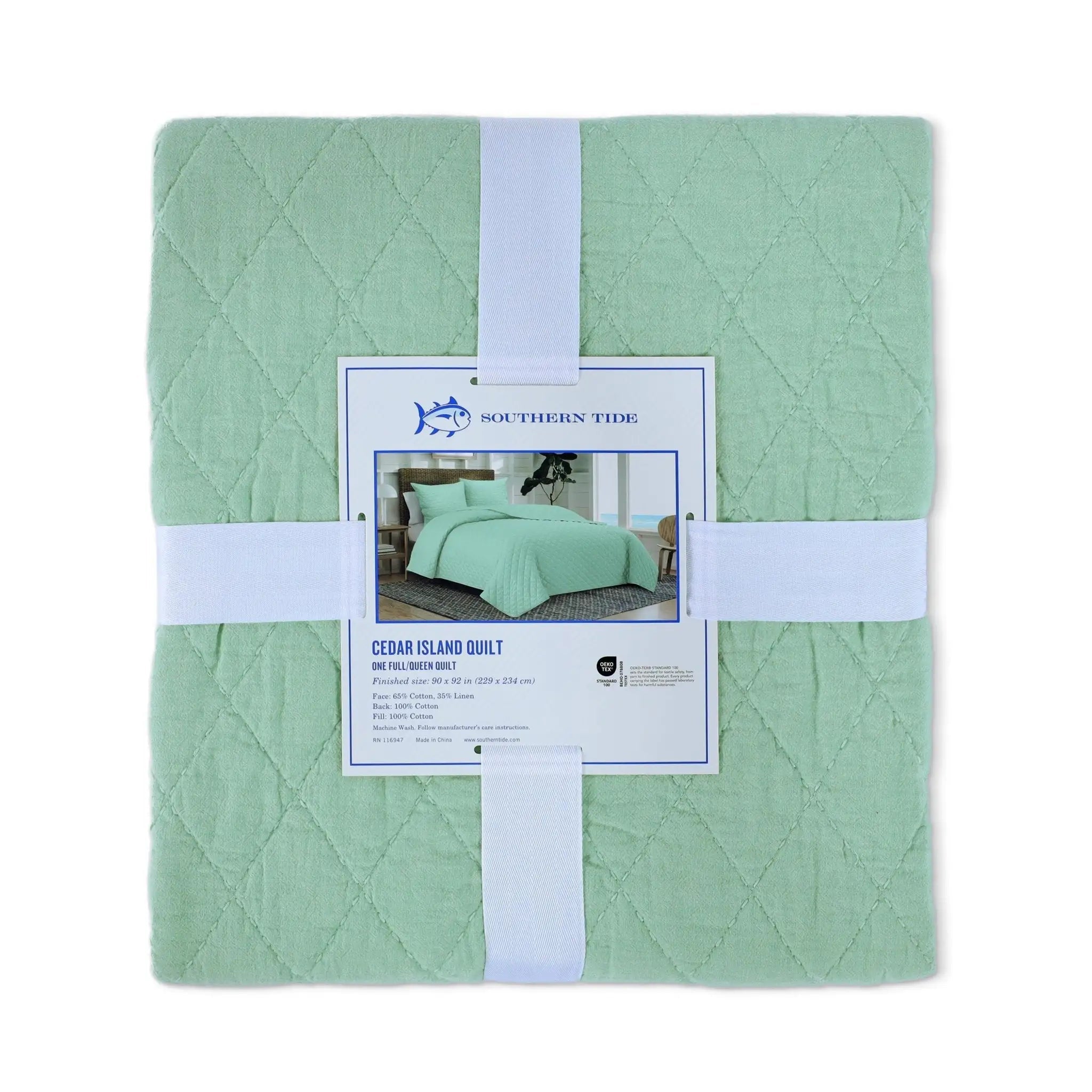 A folded sage green quilt from Southern Tide, wrapped in white bands with a product label in the center, on a white background.